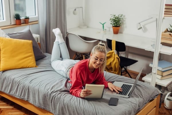 Student lying on her bed with laptop and a book